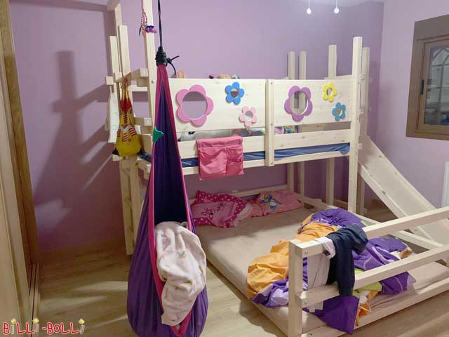 Pictured is the Bunk Bed Laterally Staggered. It is mounted at initial heights 1 and 4 since the children are still young. At the customer’s request, the lower sleeping level has been equipped with a mattress size of 140 x 200, while the upper sleeping level is 90 x 200. The ladder is attached to one short side and the slide tower is mounted to the other. After ordering the bed without any wood finish, the customers applied a white glaze.